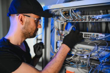 Bir teknisyen veri merkezinde sunucu ekipmanlarıyla çalışıyor. Bir adam sunucu odasında kabloları değiştiriyor..