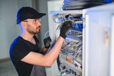 Genç adam sunucu odasında internet ekipmanı ve kablolarıyla çalışıyor..