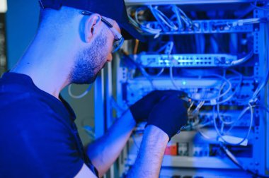 Tamirci meşgul ve sunucu odasında internet cihazları ve kablolarla çalışıyor..