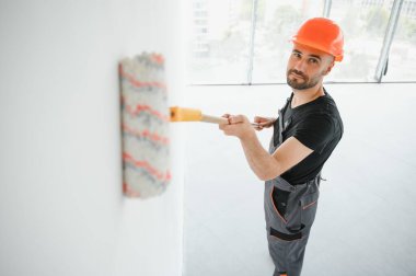 Elinde boya silindiri olan genç, neşeli profesyonel ressam. Onarım kavramı.