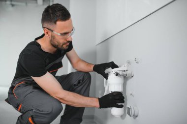 Su filtreleme sistemi kurulurken pense kullanan genç adam.