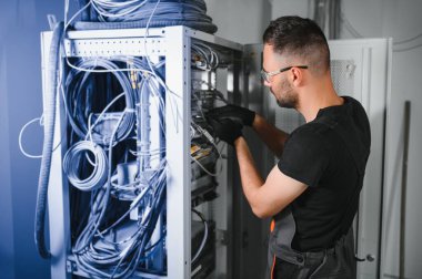 Tamirci meşgul ve sunucu odasında internet cihazları ve kablolarla çalışıyor..