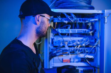 Bir teknisyen veri merkezinde sunucu ekipmanlarıyla çalışıyor. Bir adam sunucu odasında kabloları değiştiriyor..