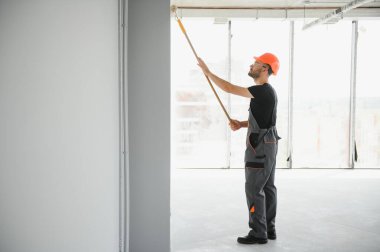 Bina müteahhidi, gri duvarı tekerlekli fırçayla boyuyor..