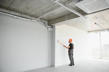 Beyaz duvar boyarken boya silindiri tutan ve yenileme yapan adamın portresi.