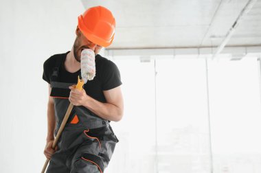 Komik ve neşeli işçi duvarları boyamak için bir silindir içinde şarkı söylüyor..