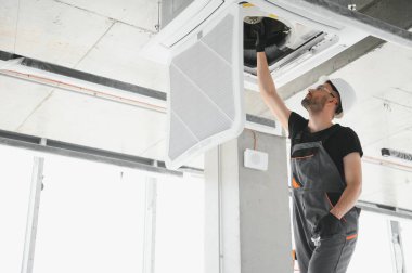 İşçi tavan havalandırma ünitesini tamir ediyor.