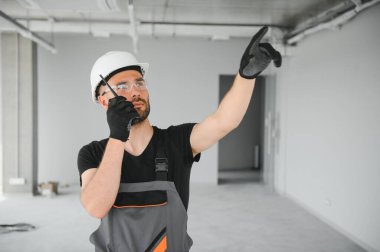 Foreman güvenlik kaskı takıyor ve inşaat alanındaki ekiple iletişim kurmak için telsiz kullanıyor..