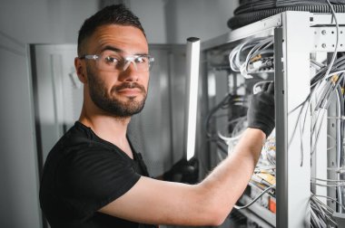 Genç adam sunucu odasında internet ekipmanı ve kablolarıyla çalışıyor..