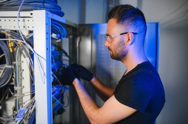 Tamirci meşgul ve sunucu odasında internet cihazları ve kablolarla çalışıyor..