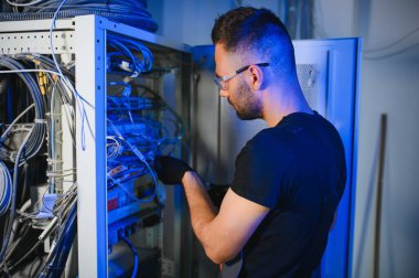 Tamirci meşgul ve sunucu odasında internet cihazları ve kablolarla çalışıyor..