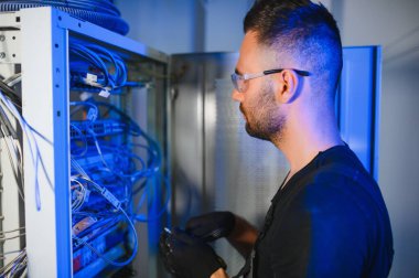 Bir teknisyen veri merkezinde sunucu ekipmanlarıyla çalışıyor. Bir adam sunucu odasında kabloları değiştiriyor..