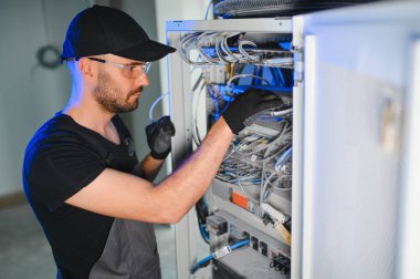 Genç adam sunucu odasında internet ekipmanı ve kablolarıyla çalışıyor..