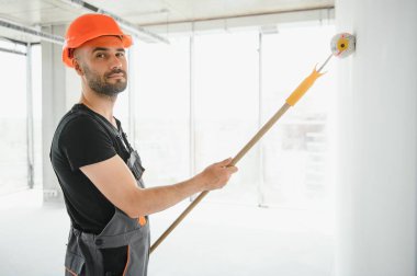 Beyaz duvar boyarken boya silindiri tutan ve yenileme yapan adamın portresi.