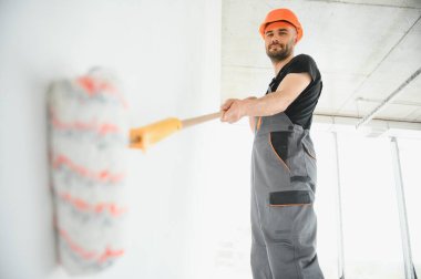 Elinde boya silindiri olan genç, neşeli profesyonel ressam. Onarım kavramı.