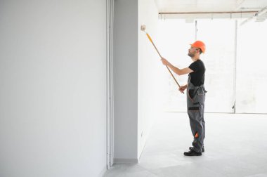 Beyaz duvar boyarken boya silindiri tutan ve yenileme yapan adamın portresi.