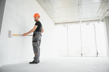 Adam duvarı boyuyor. DIY onarımı. Ressam tekerleği duvarın yanında tutuyor..