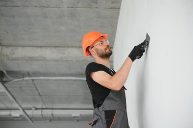 Erkek işçiler apartmanda iç yenileme yapıyorlar. Mutlu gülümseyen, kendine güvenen, beyaz üniformalı, elinde boya silindiri ve tepsisiyle kameraya bakan yetişkin duvar ressamı portresi.