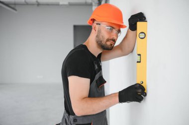 Erkek işçiler apartmanda iç yenileme yapıyorlar. Mutlu gülümseyen, kendine güvenen, beyaz üniformalı, elinde boya silindiri ve tepsisiyle kameraya bakan yetişkin duvar ressamı portresi.