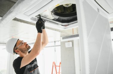 İşçi tavan havalandırma ünitesini tamir ediyor.