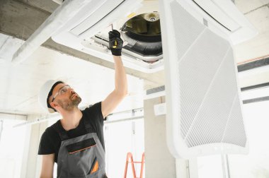 İşçi tavan havalandırma ünitesini tamir ediyor.