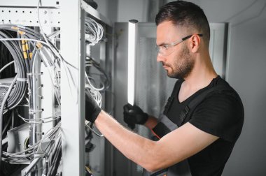 Genç adam sunucu odasında internet ekipmanı ve kablolarıyla çalışıyor..