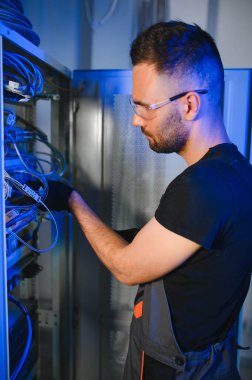 Bir teknisyen veri merkezinde sunucu ekipmanlarıyla çalışıyor. Bir adam sunucu odasında kabloları değiştiriyor..