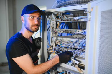 Tamirci meşgul ve sunucu odasında internet cihazları ve kablolarla çalışıyor..