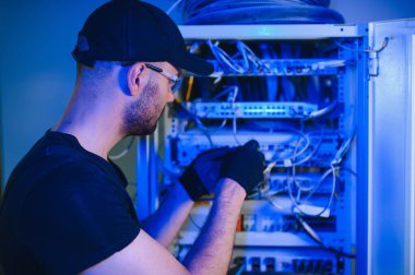Tamirci meşgul ve sunucu odasında internet cihazları ve kablolarla çalışıyor..