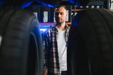 Otomobil satış departmanından yeni lastikler alırken marka ve ürün özelliklerini inceleyen genç adam portresi. Erkek müşteri araba aksesuarlarını seçiyor..