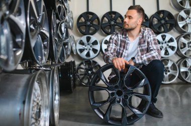 Erkek müşteri araba tamir servisinde veya oto dükkanında alaşımlı tekerlek jantları seçiyor.