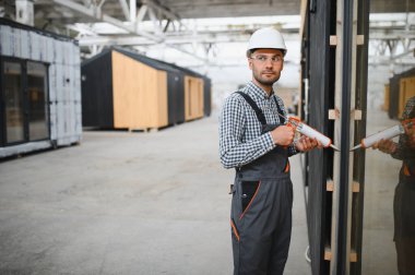 Bir işçi prefabrik modüler evdeki kuşak ve pencere çerçevesi arasındaki boşluğu doldurmak için poliüretan köpük uyguluyor..