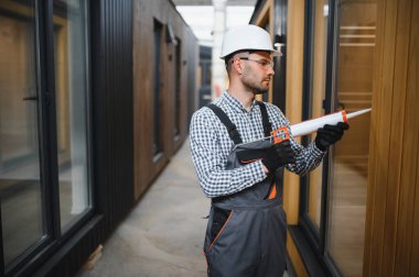 Bir işçi prefabrik modüler evdeki kuşak ve pencere çerçevesi arasındaki boşluğu doldurmak için poliüretan köpük uyguluyor..