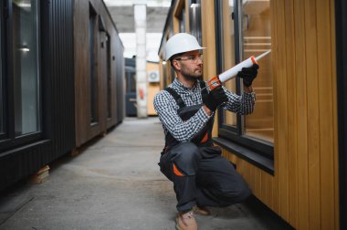 Bir işçi yeni bir modüler eve pencere takıyor. Yeni ev kavramı..