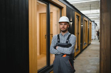 Modüler evlerin inşaat alanında miğfer takmış genç bir marangoz portresi..