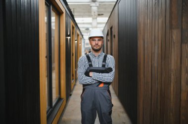 Modüler evlerin inşaat alanında miğfer takmış genç bir marangoz portresi..