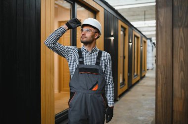 Modüler evlerin inşaat alanında miğfer takmış genç bir marangoz portresi..