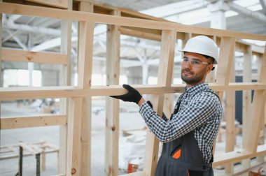 Üniformalı bir işçi ya da mühendis ahşap modüler evler için inşaat alanında çalışıyor..