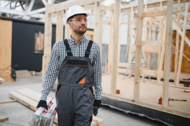 Modüler evlerin inşaat alanında miğfer takmış genç bir marangoz portresi..