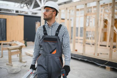 Üniformalı bir işçi ya da mühendis ahşap modüler evler için inşaat alanında çalışıyor..