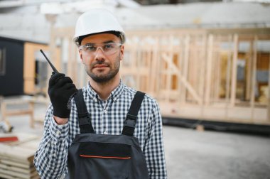 Modüler evlerin inşaat alanında miğfer takmış genç bir marangoz portresi..