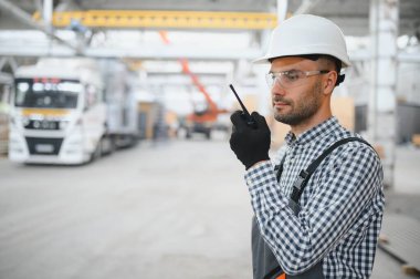 Bir mühendis modüler evlerin üretimini kontrol ediyor ve bir telsiz kullanıyor..