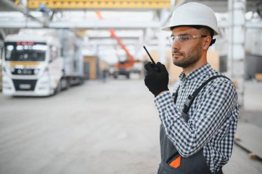 Bir mühendis modüler evlerin üretimini kontrol ediyor ve bir telsiz kullanıyor..