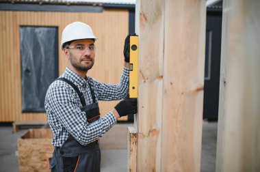 Modüler evlerin inşaat alanında miğfer takmış genç bir marangoz portresi..