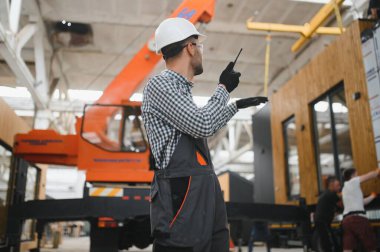 Foreman telsiz kullanarak prefabrik modüler bir evi kamyondan kamyona yüklüyor..