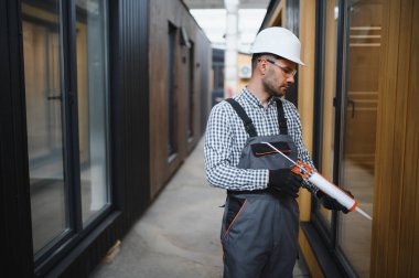 Bir işçi prefabrik modüler evdeki kuşak ve pencere çerçevesi arasındaki boşluğu doldurmak için poliüretan köpük uyguluyor..