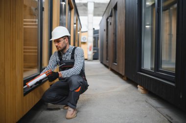 Bir işçi prefabrik modüler evdeki kuşak ve pencere çerçevesi arasındaki boşluğu doldurmak için poliüretan köpük uyguluyor..