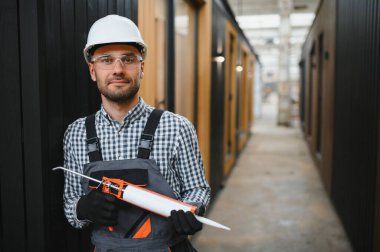 Modüler evlerin inşaat alanında miğfer takmış genç bir marangoz portresi..