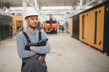 Modüler evlerin inşaat alanında miğfer takmış genç bir marangoz portresi..