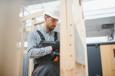 Üniformalı bir işçi ya da mühendis ahşap modüler evler için inşaat alanında çalışıyor..